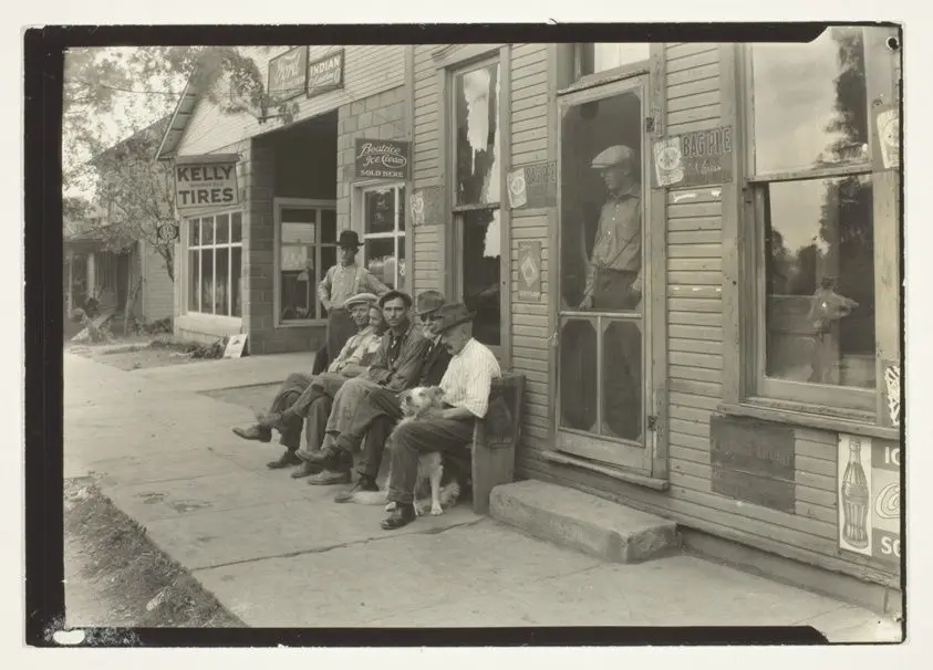 Men With Dog Sitting On Bench In Front Of General Store by Lewis Wickes Hine