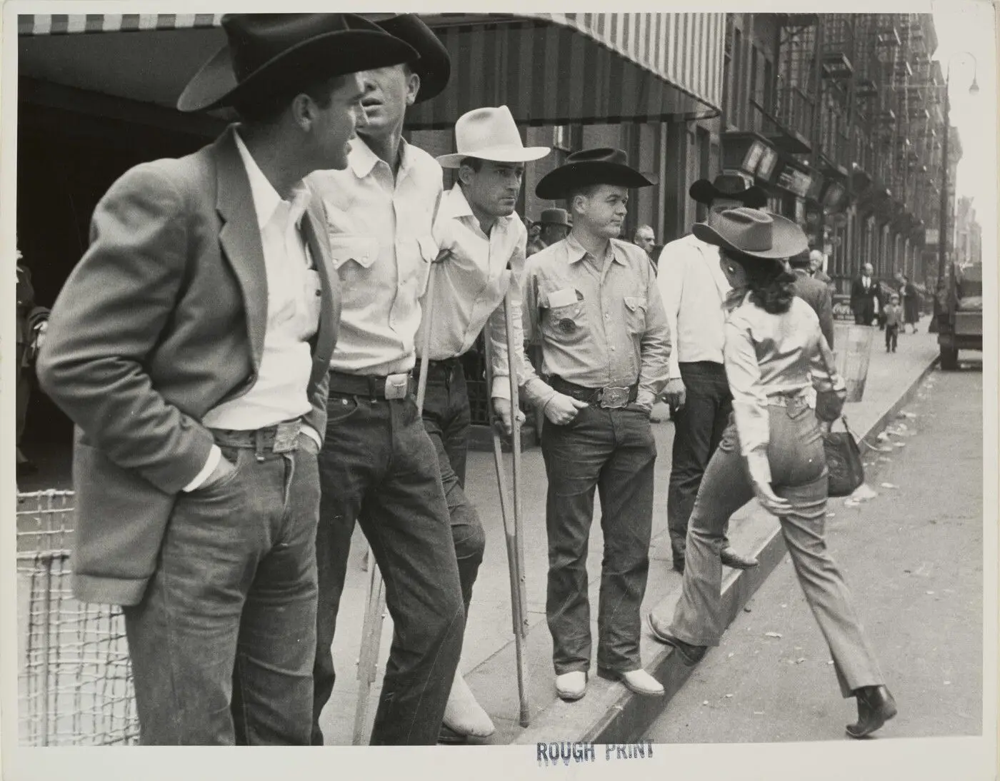 [June Ivory, trick rider, crossing the street next to a group of cowboys, Madison Square Garden Rodeo] by Robert Frank