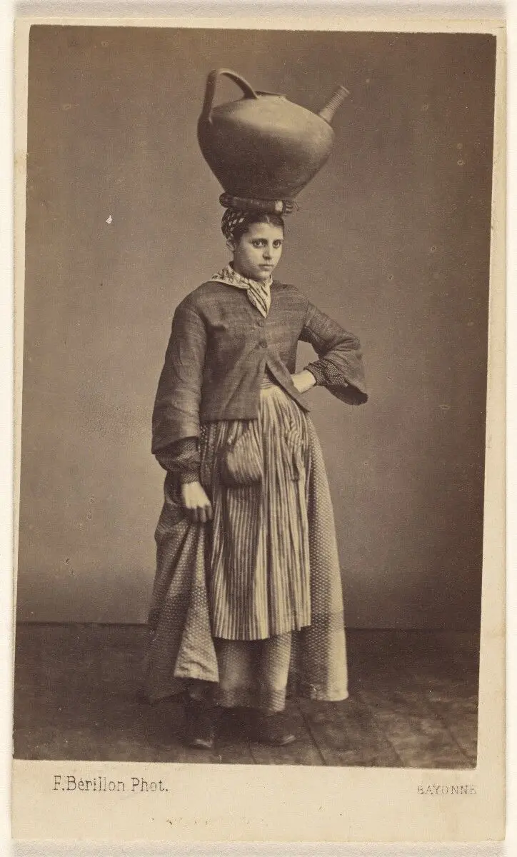 [Unidentified woman of Bayonne, France, wearing her native costume, standing, with a large ceramic pitcher on her head] by Ferdinand Berillon