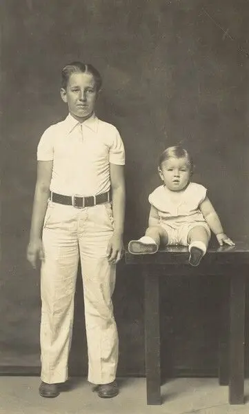 Untitled (older boy, standing, with toddler, seated on table) by Mike Disfarmer