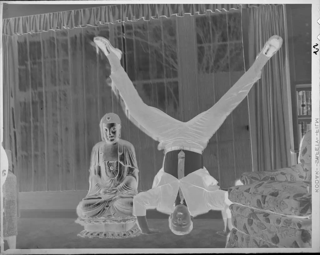 Untitled (man doing headstand next to Buddha statue) by Lucian and Mary Brown