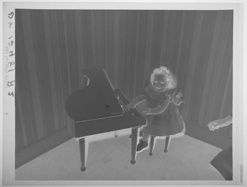 Untitled (little girl in dress playing miniature piano, looking at camera) by Paul Gittings