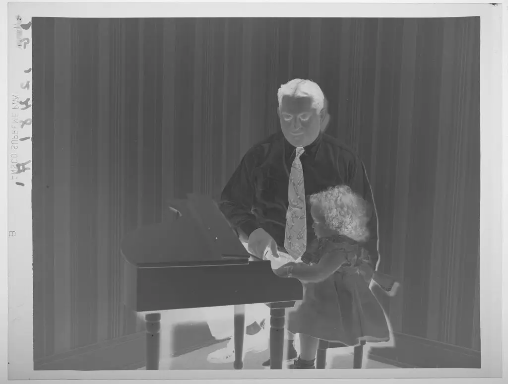 Untitled (father kneeling by little girl seated at miniature piano) by Paul Gittings