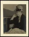 [Janet Flanner, full length portrait, seated, wearing top hat decorated with masks] by Abbott by Abbott