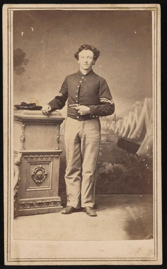 [Unidentified corporal in Union uniform holding a small pistol in front of painted backdrop showing military camp] by Ball, James Presley, 1825-1904, photographer by Ball, James Presley, 1825-1904, photographer