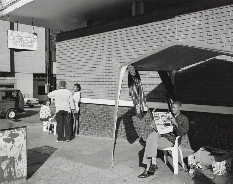 A barber under his canopy and with a connection to electricity on Smit Street, Hillbrow, Johannesburg, 19 May 1999 by David Goldblatt