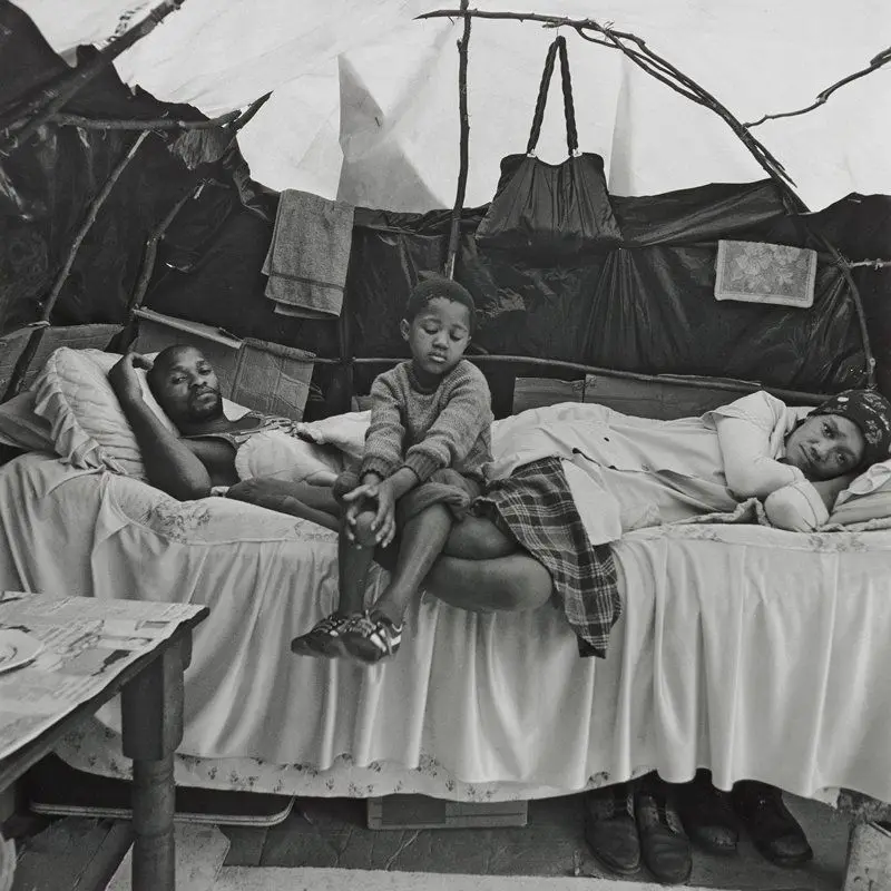 A Transkei family in their shelter, KTC squatter camp. The framework was made of strips of Port Jackson bush. For privacy black plastic sheets were used around the lower part of the shelter. For light, translucent plastic was used on the dome. Cape Town, September 1984 by David Goldblatt
